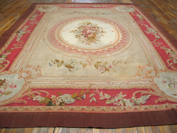 Large, low-pile rug featuring an ivory field, central floral medallion, and ornate pink and coral borders on a wood floor.