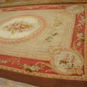 Low-pile rug with a cream and pink floral medallion and coral-red borders on wooden planks.