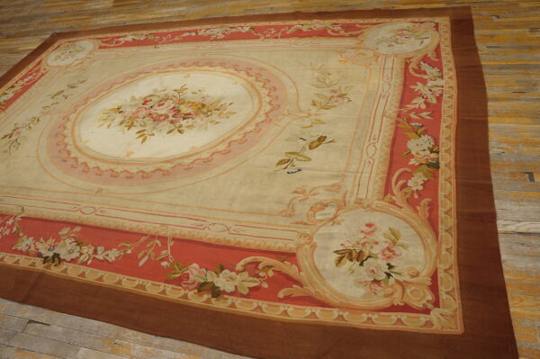 Low-pile rug with a cream and pink floral medallion and coral-red borders on wooden planks.