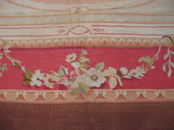 A tapestry-style rug detail features floral sprays on a salmon-pink ground bordered by pale stripes and brown trim.