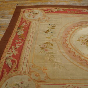 Low-pile rug with a beige floral medallion and coral border on distressed yellow-gold wooden plank flooring.