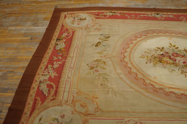 Low-pile rug with a beige floral medallion and coral border on distressed yellow-gold wooden plank flooring.