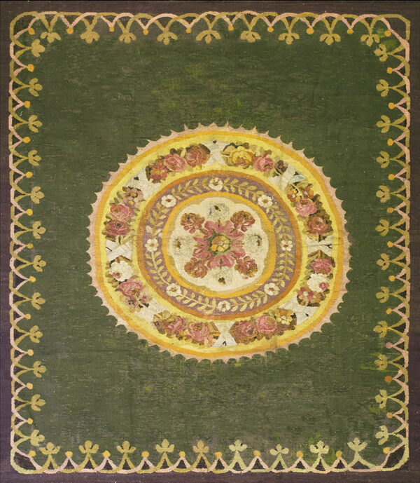 Green rug with a large circular pink and yellow floral medallion and repeating scalloped outer border.