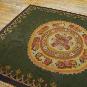 A large green rug with an elaborate circular floral design rests on worn plank wood flooring.
