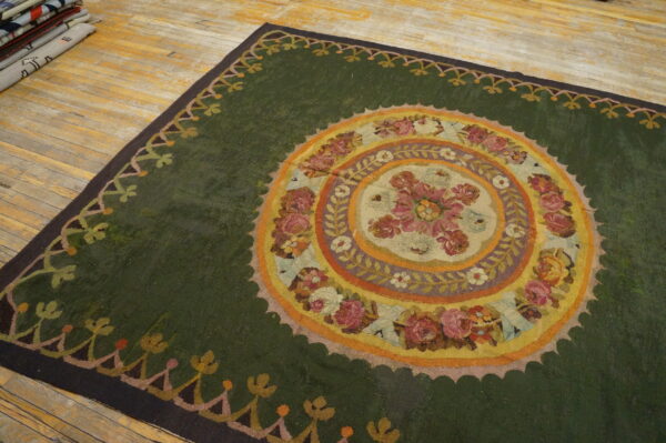 A large green rug with an elaborate circular floral design rests on worn plank wood flooring.