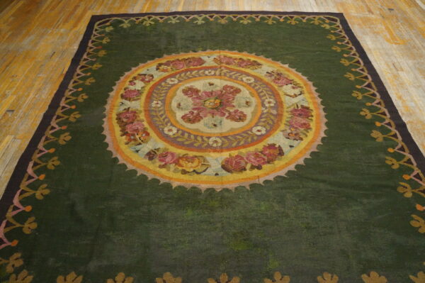 Dark green area rug featuring a central multicolored floral medallion and decorative scalloped borders on wood floor.