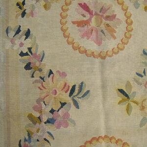 Beige flatweave rug with multicolor floral garlands and a beaded medallion on exposed wood flooring.