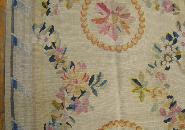 Beige flatweave rug with multicolor floral garlands and a beaded medallion on exposed wood flooring.