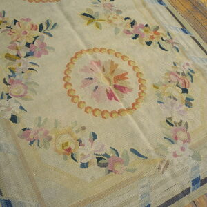 Light beige flatweave rug featuring a central floral medallion and garlands, set on rough wooden plank flooring.