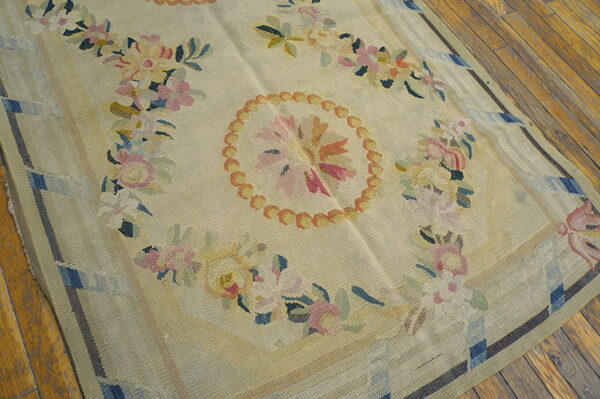 Light beige flatweave rug featuring a central floral medallion and garlands, set on rough wooden plank flooring.