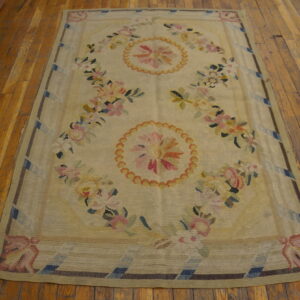 Pale yellow flatweave rug featuring pink and blue floral medallions rests on rustic wood planks.
