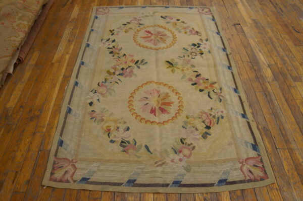 Pale yellow flatweave rug featuring pink and blue floral medallions rests on rustic wood planks.