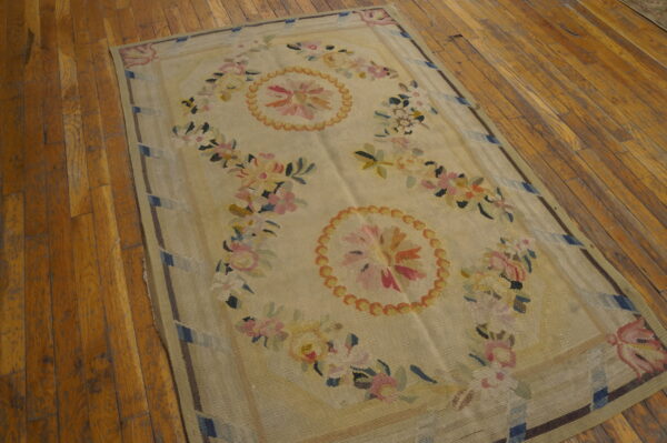 Floral flatweave rug featuring colorful pink and yellow designs on a pale field over wood floors.