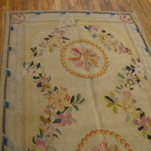 Pale flatwoven rug with pink and yellow floral patterns rests on distressed wooden floorboards.