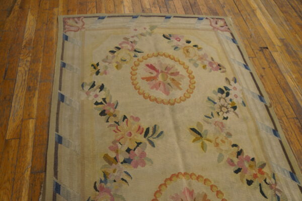 Pale flatwoven rug with pink and yellow floral patterns rests on distressed wooden floorboards.