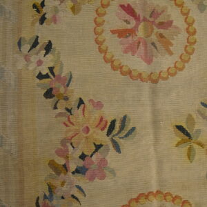 Textured beige flatweave rug featuring pale pink and orange floral garlands next to distressed hardwood flooring.