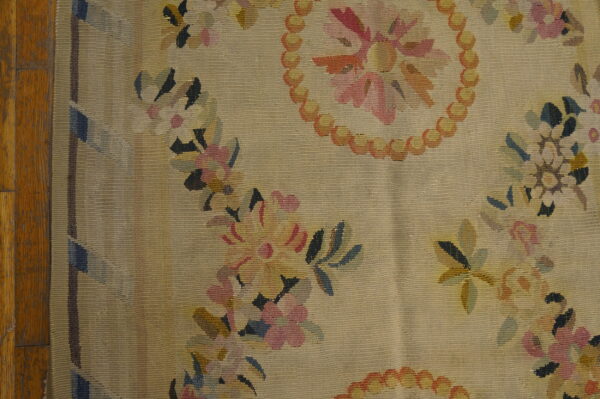 Textured beige flatweave rug featuring pale pink and orange floral garlands next to distressed hardwood flooring.