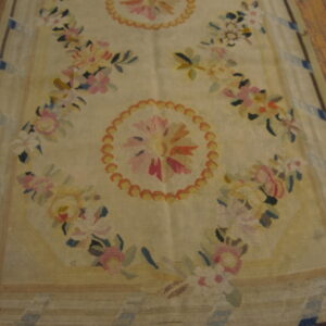 Beige rug featuring repeated pink, yellow, and blue floral medallions and garlands on wood flooring.