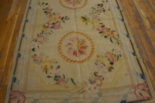 Beige rug featuring repeated pink, yellow, and blue floral medallions and garlands on wood flooring.