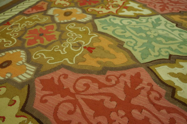 Flat-woven rug displaying large terracotta, olive, and mint panels with detailed scrolling floral patterns.