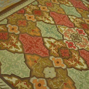 Rust, olive, orange, and sage geometric tile pattern rug displayed on light distressed wooden floor.