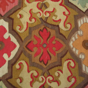 Close-up detail of a flatweave rug with interlocking geometric medallions in red, brown, yellow, and beige.