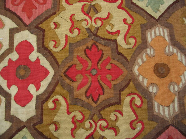 Close-up detail of a flatweave rug with interlocking geometric medallions in red, brown, yellow, and beige.