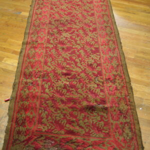 Distressed red and olive runner rug with high texture lies on warm light brown hardwood floors.