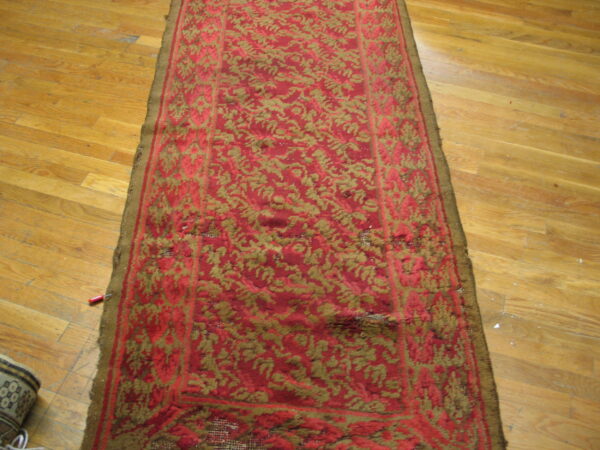 Distressed red and olive runner rug with high texture lies on warm light brown hardwood floors.