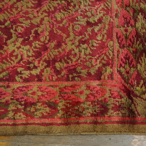 Plush red and khaki floral pattern rug border sitting on light wooden floorboards.