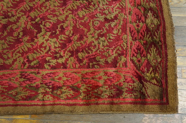 Plush red and khaki floral pattern rug border sitting on light wooden floorboards.