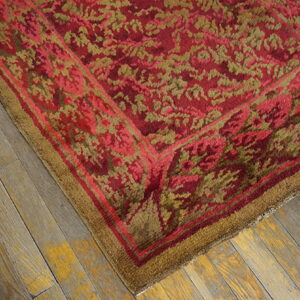 Textured red and moss green rug with a floral pattern and wide border rests on rustic wood planks.