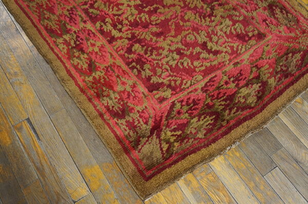 Textured red and moss green rug with a floral pattern and wide border rests on rustic wood planks.