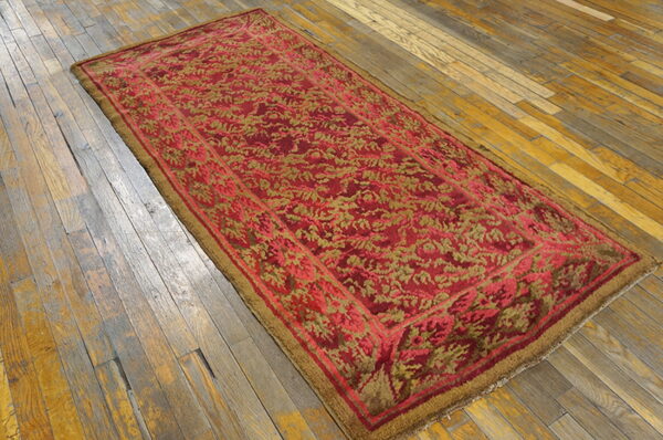Red and gold floral patterned runner rug displayed on distressed, wide-plank wood flooring.