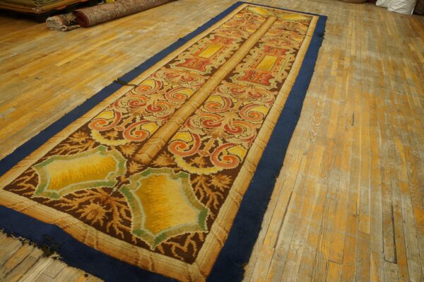 Ornate gold, orange, and brown runner rug with a navy border lies on distressed wooden flooring.