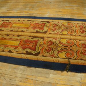 Ornate yellow, red, and orange runner rug with a dark blue border lying on distressed wood planks.
