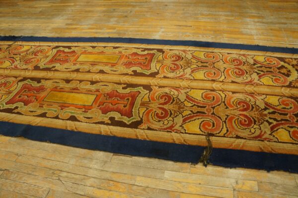 Ornate yellow, red, and orange runner rug with a dark blue border lying on distressed wood planks.