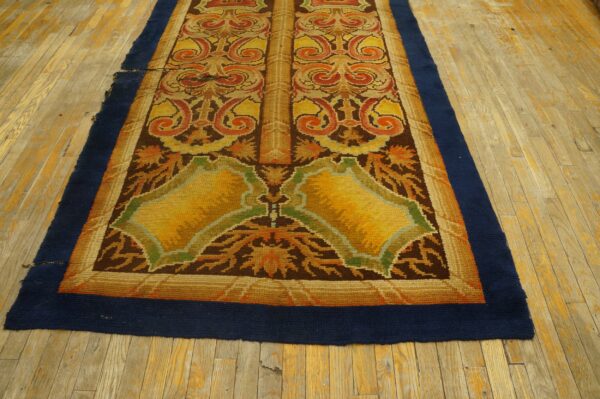 Ornate runner rug in gold, brown, and rust with a navy border lying on distressed light wood floors.