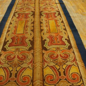 Symmetrical runner rug with baroque scrolling patterns in gold, rust, and brown on aged wooden floors.