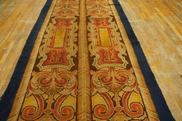 Symmetrical runner rug with baroque scrolling patterns in gold, rust, and brown on aged wooden floors.