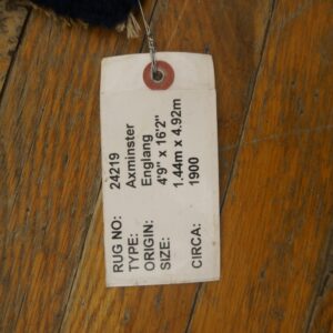 Dark blue high-pile rug corner rests on rustic wood flooring, tagged with a white label.