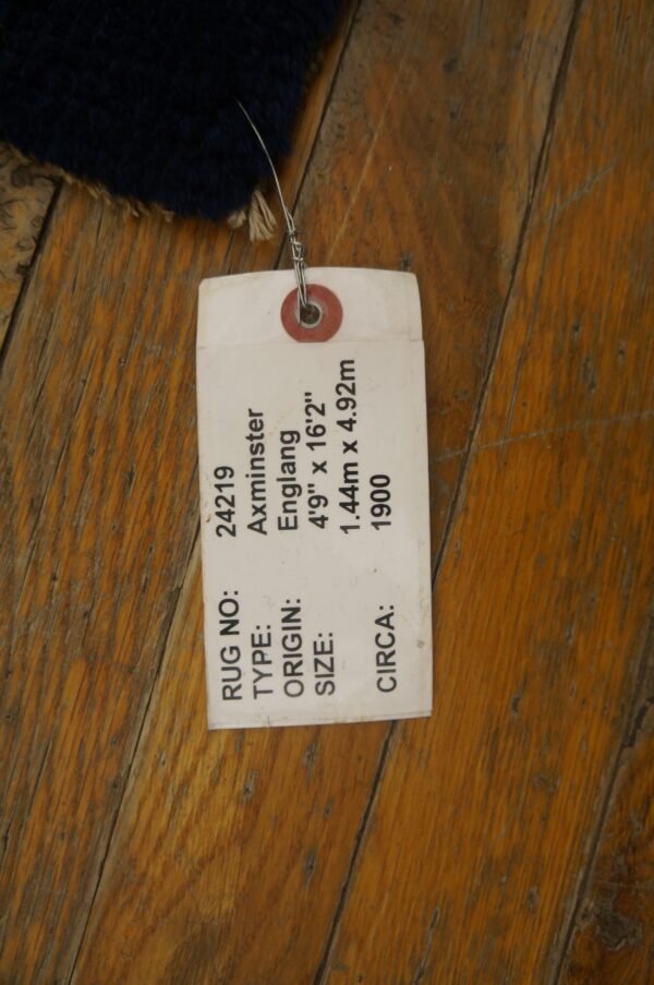 Dark blue high-pile rug corner rests on rustic wood flooring, tagged with a white label.