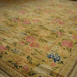 Large gold rug featuring an all-over traditional floral design in pink, blue, and cream on wood flooring.