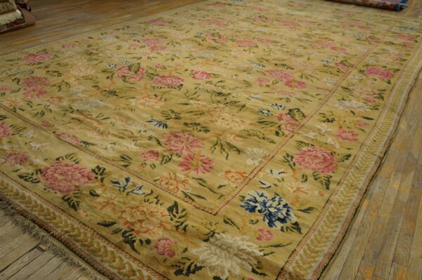 Large gold rug featuring an all-over traditional floral design in pink, blue, and cream on wood flooring.