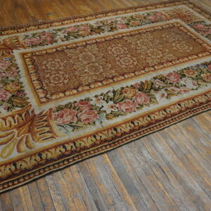 Low-pile rug in gold, rust, and cream featuring floral borders sits on distressed wood plank flooring.