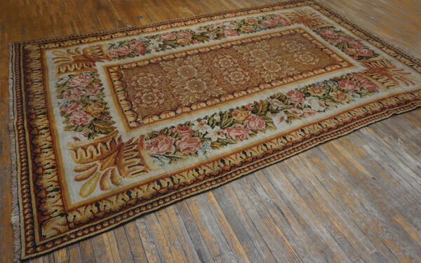 Low-pile rug in gold, rust, and cream featuring floral borders sits on distressed wood plank flooring.