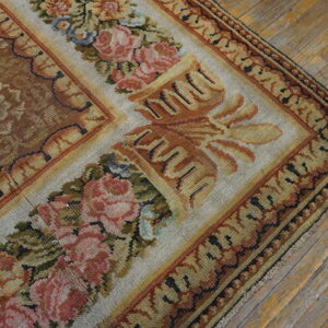 Muted floral rug corner showing a brown field and rose-patterned border resting on distressed wood planks.