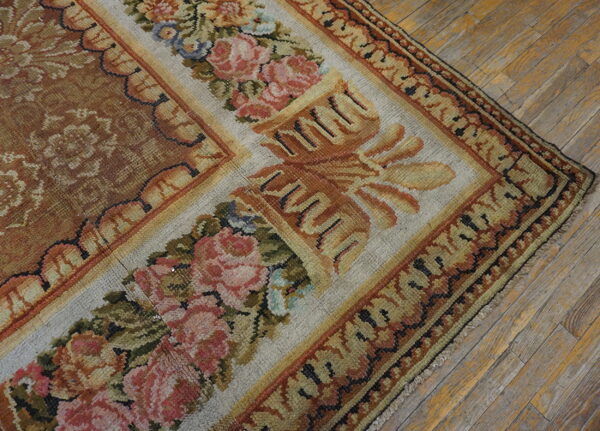 Muted floral rug corner showing a brown field and rose-patterned border resting on distressed wood planks.