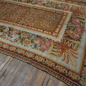 Ornate floral rug with rose borders and a brown center covers weathered, wide-plank wood floors.