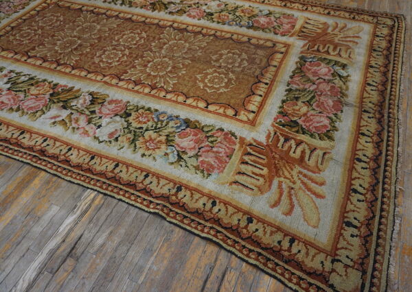 Ornate floral rug with rose borders and a brown center covers weathered, wide-plank wood floors.